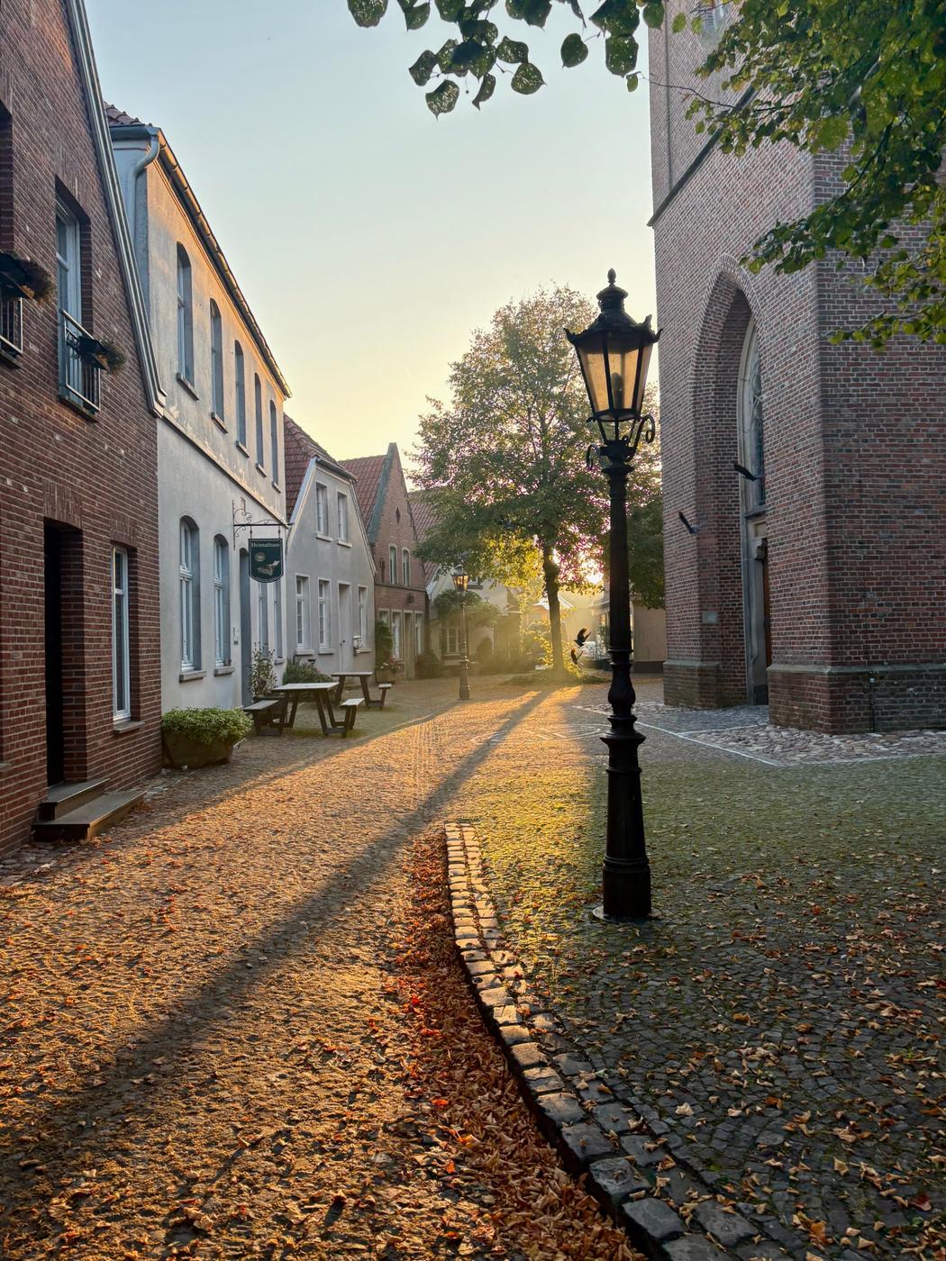 Der Kring in Ammeloe im Morgenlicht mit Laterne, Kirche und Pflasterweg